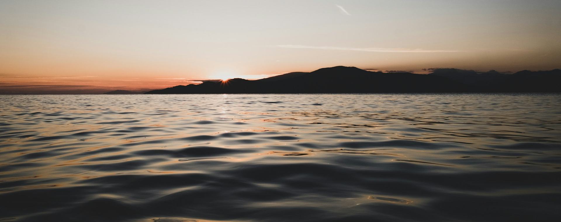 The sun setting behind a coastal mountain ridge across open water near Vancouver